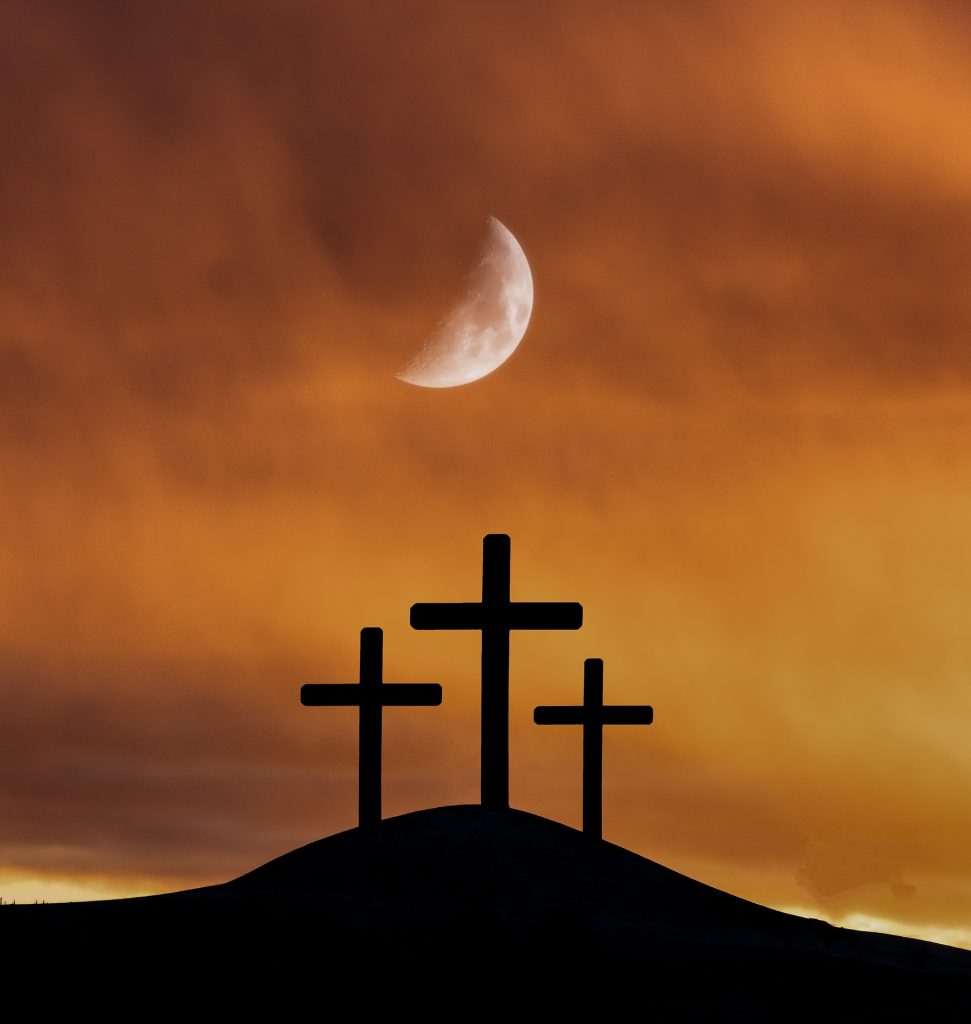 3 crosses on a hill silhouetted with the moon above and a golden sky